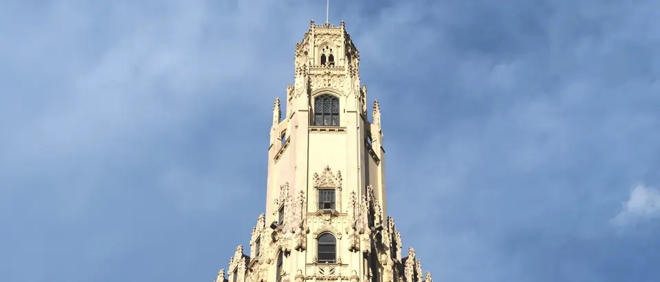 The Gothic Revival tower of the Emily Morgan building in San Antonio with a Texas flag on top, under a blue sky