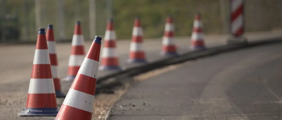 A line of red and white traffic cones along the curving edge of a road under repair