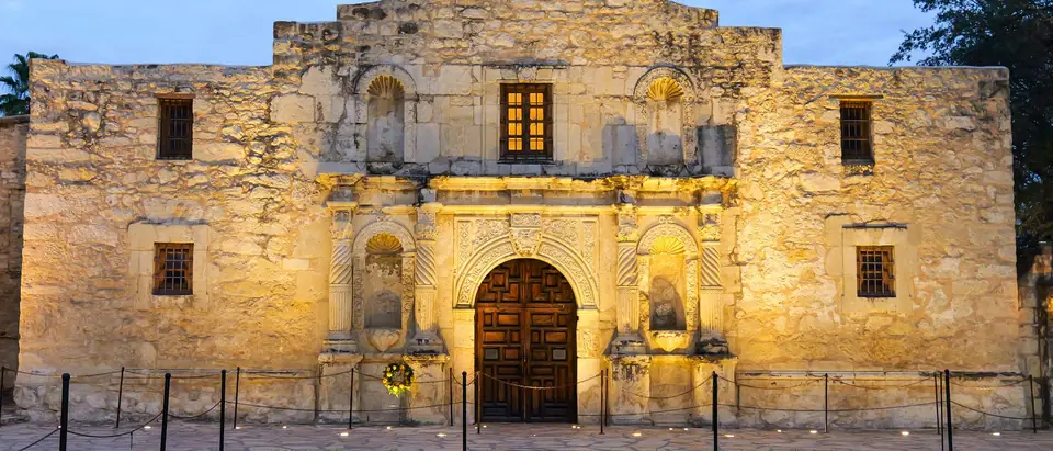 The Alamo's church front softly lit at dusk under a blue sky