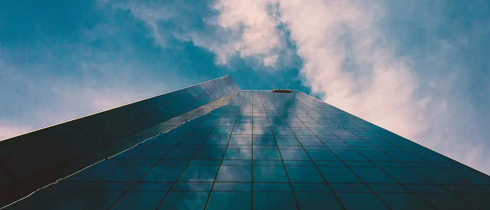 Looking up a glass skyscraper in San Antonio that reflects blue sky and pink clouds