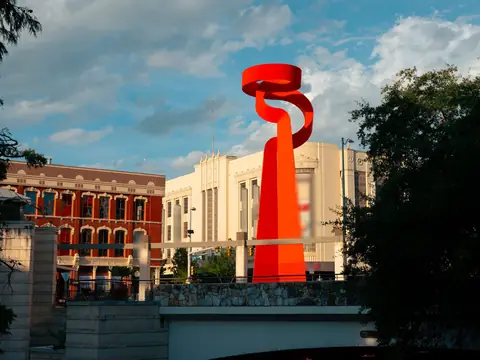 La Antorcha de la Amistad, the tall red sculpture in downtown San Antonio, beside historic buildings in daylight