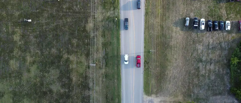 A two-lane road seen straight down from a drone, passing fields and a small parking lot in Royse City, Texas