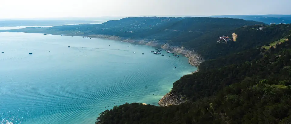A Texas lake seen from a high bluff, turquoise water below wooded Hill Country ridges