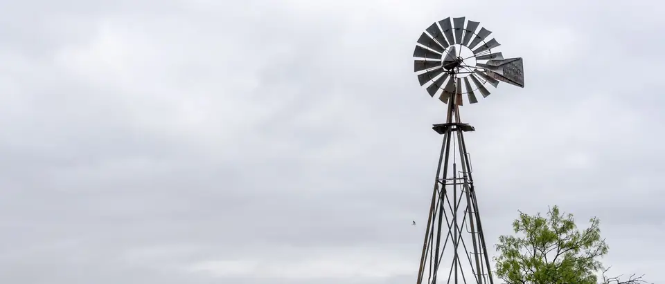 An old metal windmill beside a mesquite tree on open Texas ranch land under grey clouds near Abilene